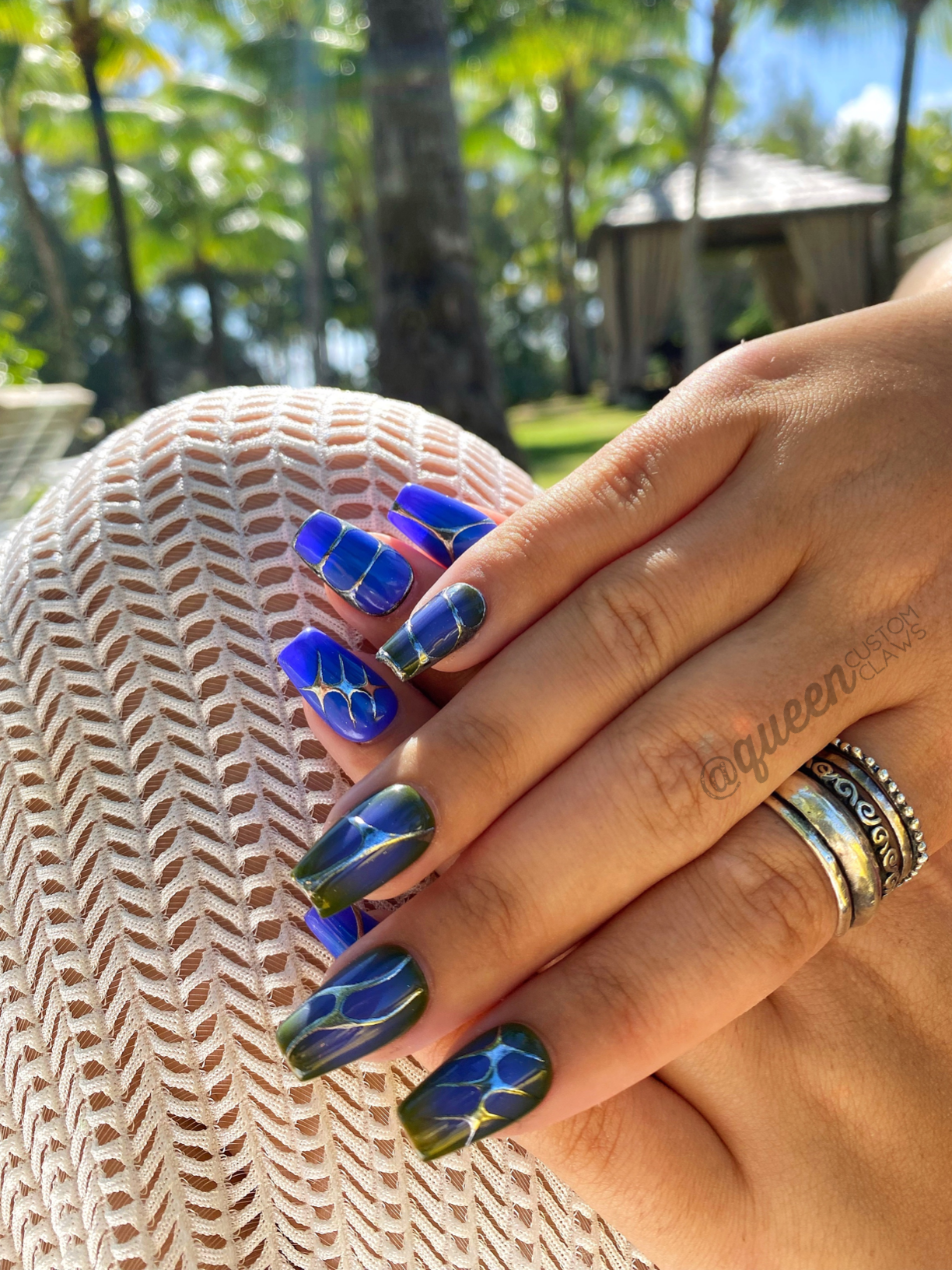 hand held up, modeling custom made press on nails with an aura heart, and 90's tribal chrome designs in silver. each nail has a different design in chrome. the nail base is purple, with an airbrushed center in a darker blue over the purple base. the other hand is olive green and purple base colors under the silver designs