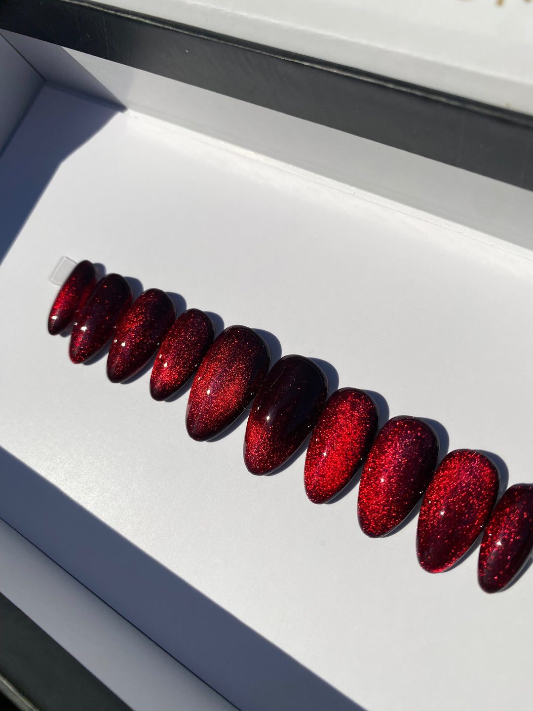 Magnetic Sparkle press-on nails give you that dazzling 3D cats eye effect with a glossy magnetic gel polish.. red magnetic cat eye polished press on nails in almond shape