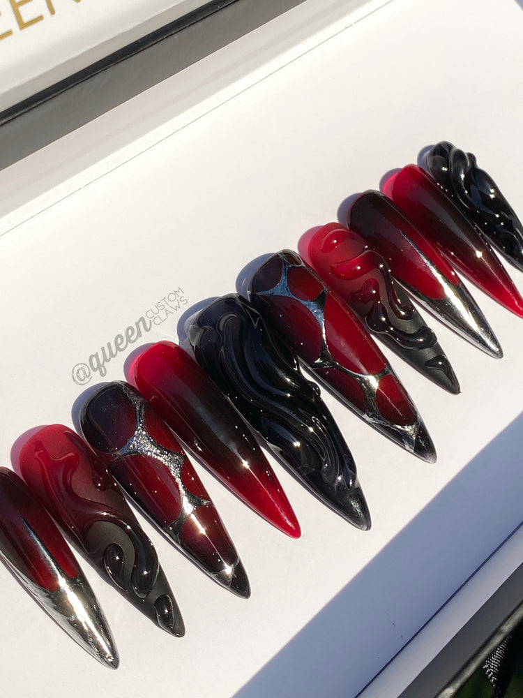 a close up of a bunch of red and black stiletto press on nails. 3d swirl gel nails