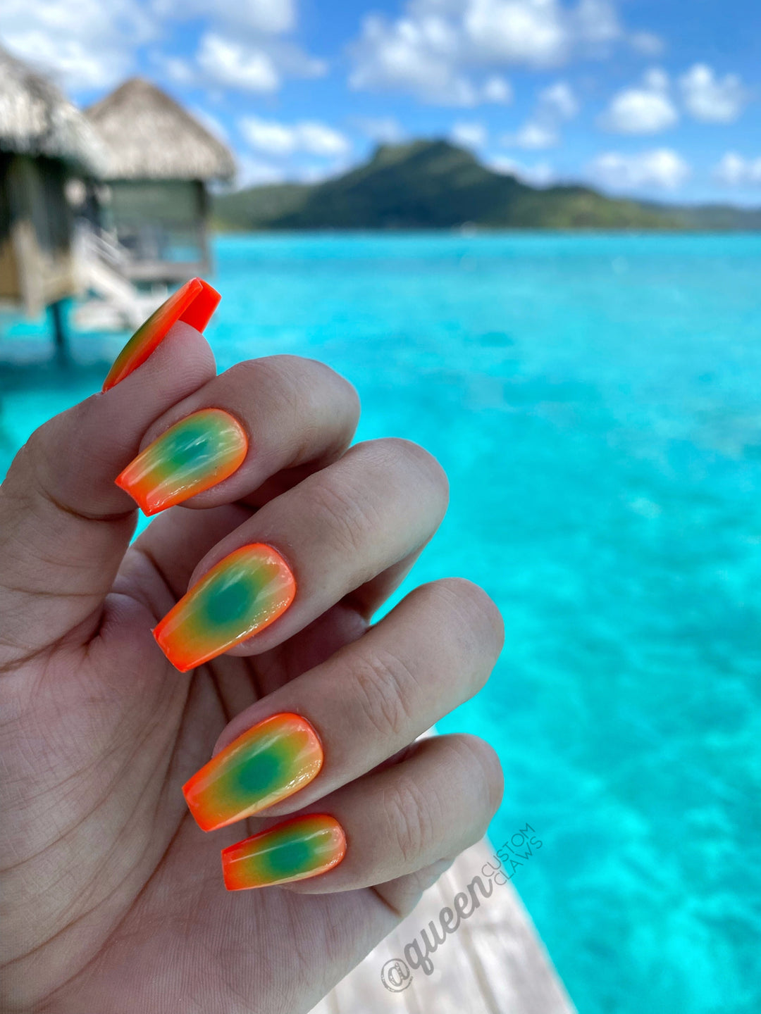 a hand modeling a bright orange and green aura manicured press on nails