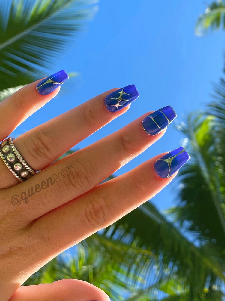 hand held up, modeling custom made press on nails with an aura heart, and 90's tribal chrome designs in silver. each nail has a different design in chrome.  the nail base is purple, with an airbrushed center in a darker blue over the purple base.