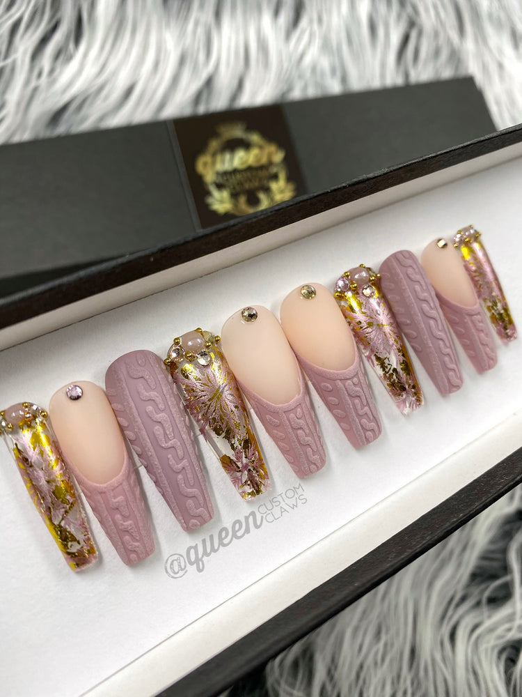 a set of pink and gold custom made press on nails . the nails are in a swather knit cable pattern with French tips and gold accent nails