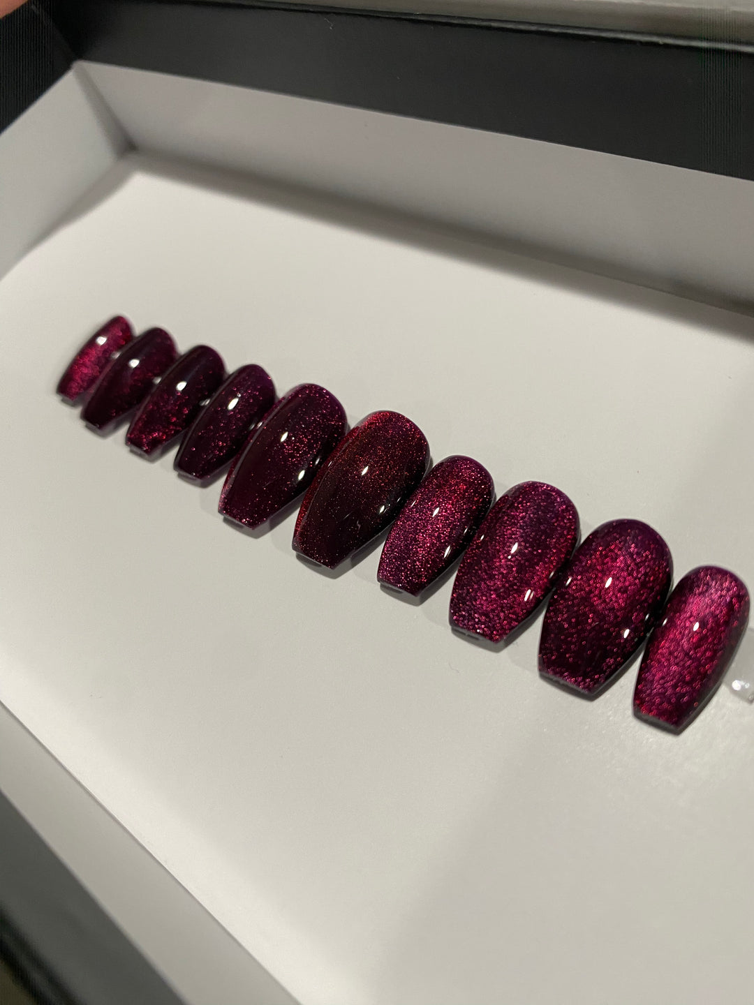 Magnetic Sparkle press-on nails give you that dazzling 3D cats eye effect with a glossy magnetic gel polish.. red magnetic cat eye polished press on nails in almond shape. purple magnetic polish
